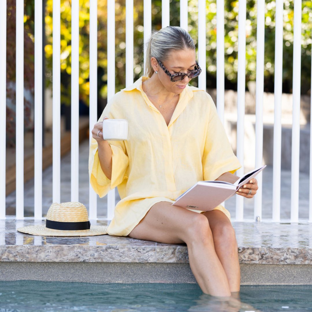 Woman with a coffee and a book sitting beside a pool fence